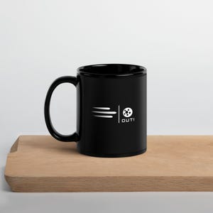 May include: Black coffee mug with a white soccer ball graphic and the word "OUT!" on the side. The mug is sitting on a wooden surface.