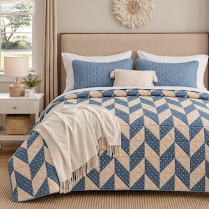 Könnte beinhalten: Ein Bett mit einer Steppdecke in einem blauen und beigen geometrischen Zickzackmuster, akzentuiert durch kleine weiße Punkte. Das Bettzeug umfasst zwei blaue Steppkissenbezüge, ein cremefarbenes rechteckiges Kissen und eine cremefarbene Decke mit Fransen.
