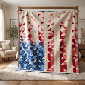 May include: A large, cream-colored quilt with a patriotic design. The quilt features a blue square with white stars and red and pink triangles arranged in vertical stripes. The quilt is displayed on a wooden bed frame.