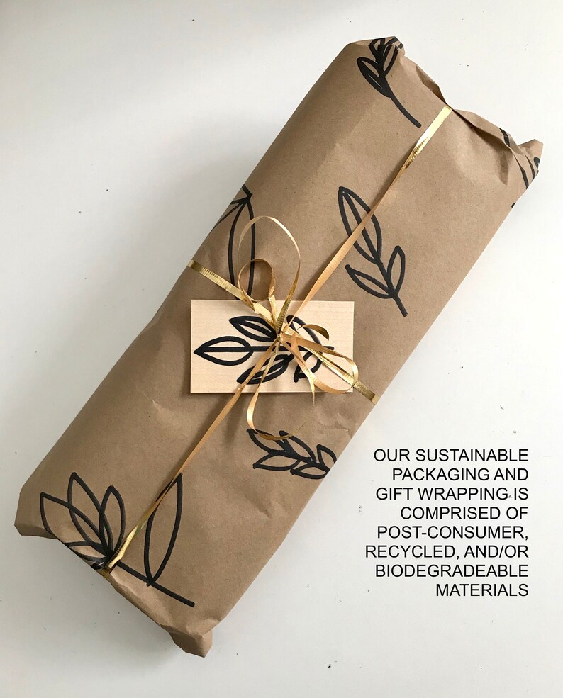 May include: A brown paper gift package with a gold ribbon and a small tag. The paper has a black and white leaf pattern. The text on the tag reads: "OUR SUSTAINABLE PACKAGING AND GIFT WRAPPING IS COMPRISED OF POST-CONSUMER, RECYCLED, AND/OR BIODEGRADEABLE MATERIALS."