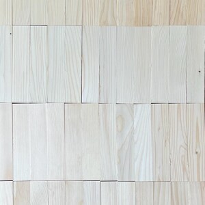 May include: A close-up of a wall made of light wood planks. The planks are arranged in a staggered pattern, creating a textured surface.