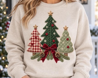 May include: A beige crewneck sweatshirt featuring a central graphic of three stylized Christmas trees. The trees are decorated with red buttons, gold stars, and white snowflake accents. A large red velvet bow sits at the base.