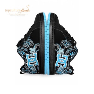 Puede incluir: Un par de zapatillas negras con un logotipo DC azul claro en el lateral, acentuado con intrincados patrones florales en blanco y azul claro. Los zapatos tienen cordones negros, una parte superior negra y una entresuela de color azul claro.