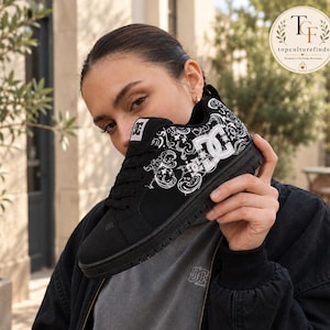 Puede incluir: Una zapatilla baja negra con un logotipo DC blanco en el lateral y un intrincado patrón de estilo cachemir blanco en la parte superior. El calzado cuenta con cordones negros, suela negra y un cuello acolchado de diseño clásico.