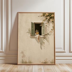 May include: A framed wall art print depicting a beige stucco building facade with an open window. A person wearing a hat and white clothing sits on the window ledge reading a book. Green climbing vines with yellow flowers frame the window.