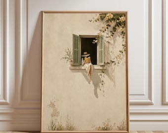 May include: A framed wall art print depicting a beige stucco building facade with an open window. A person wearing a hat and white clothing sits on the window ledge reading a book. Green climbing vines with yellow flowers frame the window.
