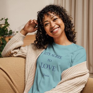 May include: A light blue t-shirt with the text "LET'S AGREE TO LOVE" and the name "Yulia" in a dark blue script. The shirt is worn with a beige cardigan.