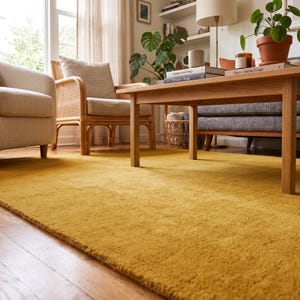 Close-up view of a handmade hand tufted mustard yellow wool area rug with a plush textured surface and neatly finished rolled edge revealing durable cotton canvas backing. Modern minimalist solid color rug crafted from premium New Zealand wool, ideal for living room, bedroom, office, nursery, luxury home decor, custom size area rug, contemporary interior, housewarming gift, and new home gift.