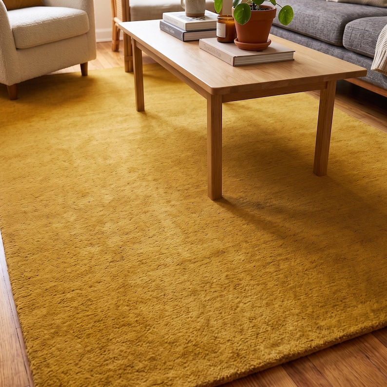 Close-up view of a handmade hand tufted mustard yellow wool area rug with a plush textured surface and neatly finished rolled edge revealing durable cotton canvas backing. Modern minimalist solid color rug crafted from premium New Zealand wool, ideal for living room, bedroom, office, nursery, luxury home decor, custom size area rug, contemporary interior, housewarming gift, and new home gift.