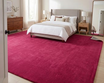 May include: A large, solid magenta area rug with a plush, textured surface covering the floor of a bedroom. The rectangular rug features a consistent deep pink hue and a soft pile, extending from the foreground toward the bed frame.