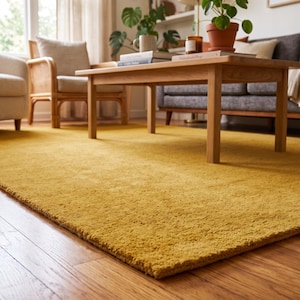 Close-up view of a handmade hand tufted mustard yellow wool area rug with a plush textured surface and neatly finished rolled edge revealing durable cotton canvas backing. Modern minimalist solid color rug crafted from premium New Zealand wool, ideal for living room, bedroom, office, nursery, luxury home decor, custom size area rug, contemporary interior, housewarming gift, and new home gift.