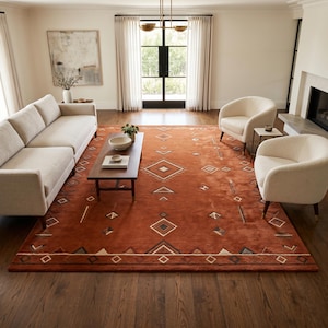 Hand tufted wool rug in rich terracotta featuring a southwestern tribal geometric pattern. Bold diamond medallion centre with concentric borders, ivory and charcoal accents, aztec-inspired motifs. Plush medium pile, artisan crafted, placed on warm oak hardwood floor. Perfect for boho living room, rustic bedroom or as a unique housewarming gift. Custom sizes available.
