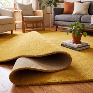 Close-up view of a handmade hand tufted mustard yellow wool area rug with a plush textured surface and neatly finished rolled edge revealing durable cotton canvas backing. Modern minimalist solid color rug crafted from premium New Zealand wool, ideal for living room, bedroom, office, nursery, luxury home decor, custom size area rug, contemporary interior, housewarming gift, and new home gift.