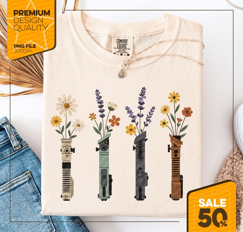 May include: Cream-colored t-shirt featuring a floral design. The graphic depicts four stylized lightsabers, each holding a different type of flower. The shirt has the words "Comfort Colors" on the tag. A gold necklace is draped across the shirt. The image also includes the text "Premium Design Quality" and "Sale 50%"