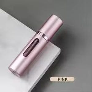 K&ouml;nnte beinhalten: Ein rosa, zylindrischer Parf&uuml;mzerst&auml;uber mit einem transparenten Fenster zur Anzeige des Inhalts. Der Zerst&auml;uber hat eine metallische Oberfl&auml;che und eine passende Kappe. Das Produkt ist mit "PINK" in einem rechteckigen Feld gekennzeichnet.