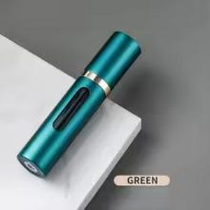 K&ouml;nnte beinhalten: Ein zylindrischer, teal-farbener Parf&uuml;mzerst&auml;uber mit einem goldfarbenen Band. Der Zerst&auml;uber hat ein kleines, rechteckiges Fenster und eine Spr&uuml;hd&uuml;se. Das Wort "GREEN" ist auf einem kleinen, rechteckigen Etikett aufgedruckt.