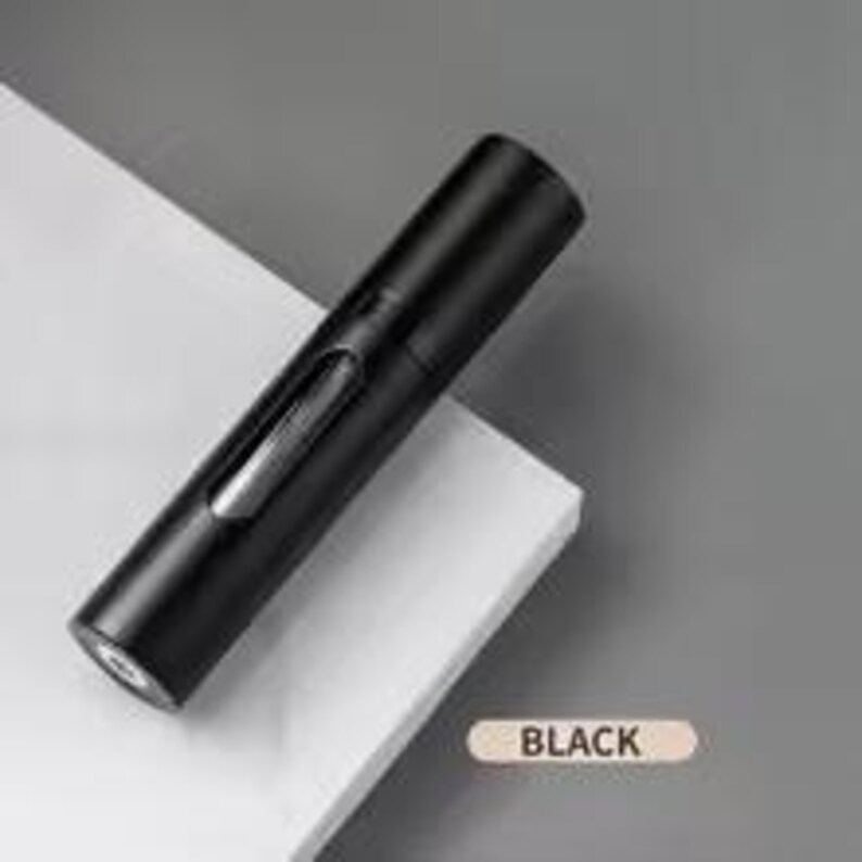 K&ouml;nnte beinhalten: Ein schwarzer, zylindrischer Wein&ouml;ffner mit einem transparenten Sichtfenster. Der &Ouml;ffner liegt auf einer wei&szlig;en Oberfl&auml;che. Das Wort "BLACK" ist auf einem kleinen, beigen Rechteck aufgedruckt.