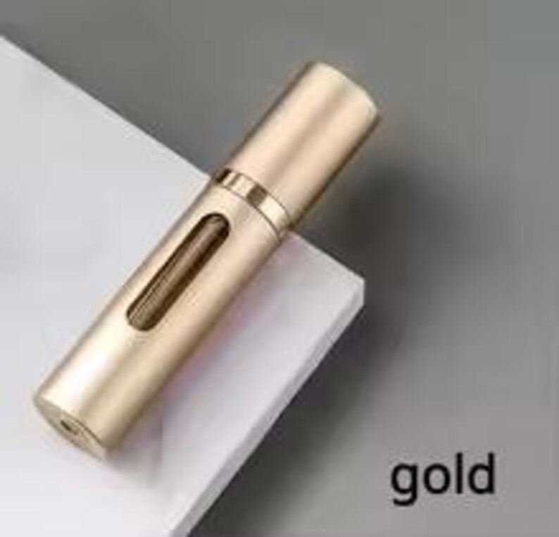 K&ouml;nnte beinhalten: Ein goldfarbener, zylindrischer Parf&uuml;mzerst&auml;uber mit einem kleinen, rechteckigen Fenster. Der Zerst&auml;uber hat eine Kappe und eine Spr&uuml;hd&uuml;se. Das Wort "gold" ist unten rechts aufgedruckt.