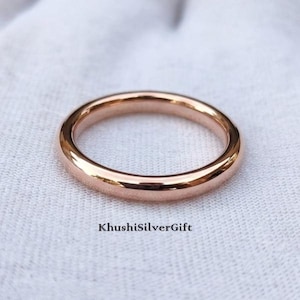 Op de afbeelding: Een gepolijste ring in roségoudkleur met een glad, afgerond profiel. De ring heeft een eenvoudig, doorlopend cirkelvormig ontwerp met een reflecterende metalen afwerking. De tekst KhushiSilverGift staat in het zwart onder de ring.
