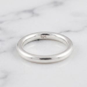 May include: A smooth, polished silver band ring with a rounded profile. The interior of the band is clearly stamped with the hallmark 925, indicating the metal composition. The ring has a simple, continuous circular shape with a reflective finish.