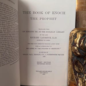 Puede incluir: Libro abierto titulado "THE BOOK OF ENOCH THE PROPHET" con texto negro. El libro est&aacute; traducido de un manuscrito et&iacute;ope y publicado en Londres en 1883. La portada de un libro dorado es visible a la derecha.