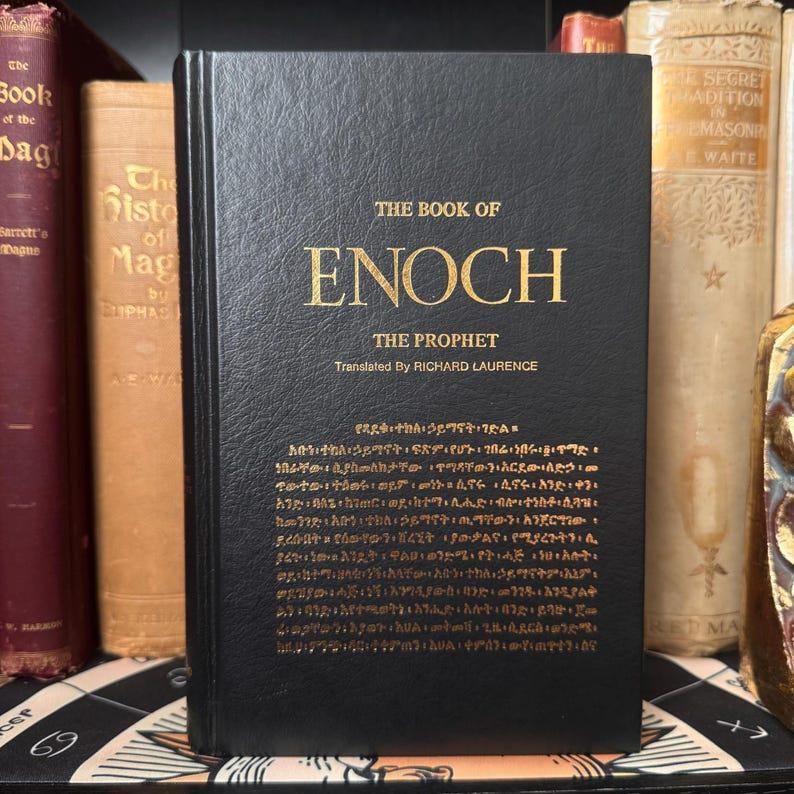 Puede incluir: Un libro de tapa dura negro titulado "THE BOOK OF ENOCH" con letras doradas. El texto "THE PROPHET" y "Translated By RICHARD LAURENCE" tambi&eacute;n est&aacute;n en oro. Texto adicional en una escritura diferente est&aacute; impreso en la parte inferior de la portada.