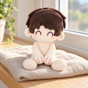 May include: A plush doll with short, dark brown hair and a light skin tone. The doll features embroidered eyes shaped like curved lines, a small mouth, and pink blush on the cheeks. It has a soft, rounded body with simple limbs and small, stitched details on the hands.
