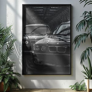May include: A black and white framed wall art print featuring two BMW automobiles positioned in a tunnel. The front-facing vehicle displays the iconic dual kidney grille and circular headlights, while the second car is visible behind it.