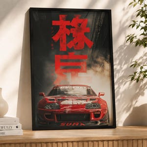 Puede incluir: Un póster vertical enmarcado que muestra un coche deportivo rojo centrado en la parte inferior, con grandes caracteres kanji rojos y texto más pequeño encima, sobre un fondo oscuro y ahumado con rayos de luz que emanan desde la parte superior.