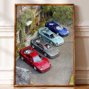 May include: A framed wall art print featuring four scale model sports cars parked in a row on a paved driveway next to a stone building. The cars are colored red, dark gray, light blue, and dark blue, each with a rear spoiler and low profile.