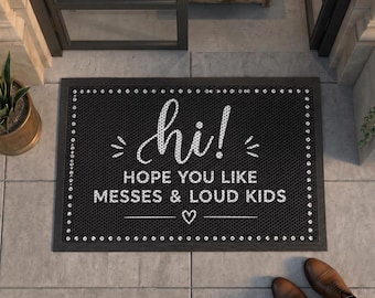 May include: A rectangular black doormat with a white border of small dots. The text reads "hi! HOPE YOU LIKE MESSES & LOUD KIDS" in a white script and sans-serif font, with a small white heart icon centered below the text on the mat surface.