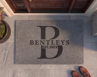 May include: A rectangular gray doormat featuring a large black letter B in the center. The text BENTLEYS is printed across the letter, with the text EST. 20XX positioned directly below it. The mat is placed on a light gray tiled entryway floor.