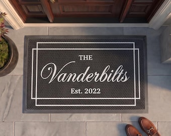May include: A rectangular black doormat with a white border consisting of two nested rectangles. The center features the white text "THE", the name "Vanderbilts" in a cursive script, and "Est. 2022" printed below in a clean, sans-serif font.