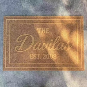 May include: A rectangular brown coir doormat featuring a double-line border. The text THE Davilas EST. 2008 is printed in the center in a combination of block and script lettering. The mat has a coarse, natural fiber texture throughout.