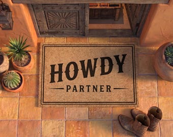 May include: A rectangular tan coir doormat featuring a black border and the text HOWDY PARTNER in a bold, western-style font. The mat is positioned on a terracotta tiled floor, surrounded by several potted succulents and a pair of brown leather boots.