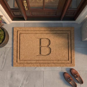 May include: A rectangular tan coir doormat featuring a large, centered, embossed letter B. The mat has a double-bordered frame design and is positioned on a light gray tiled porch floor in front of a dark wood door with a gold handle.