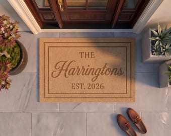 May include: A rectangular tan coir doormat featuring a dark brown double-line border. The text THE Harringtons EST. 2026 is printed in the center in a combination of serif and script fonts. The mat is positioned on a light gray tiled floor.