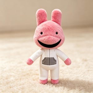 May include: A plush toy featuring a pink rabbit-like character with long ears, small black eyes, and a wide black mouth. The character is wearing a white long-sleeved jumpsuit with a gray front pocket detail and a vertical zipper line down the center.