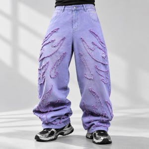 Puede incluir: Pantalones vaqueros de color lavanda con corte ancho y cintura alta. La prenda está decorada con múltiples parches en forma de llama que presentan bordes deshilachados y sin rematar en la parte delantera de ambas piernas.