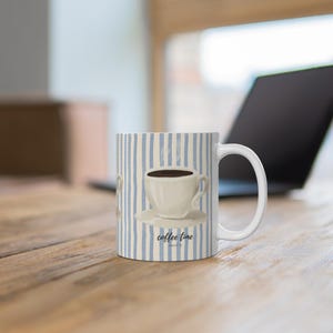 Puede incluir: Una taza de cerámica blanca con un patrón de rayas verticales de color azul claro. El centro de la taza muestra una ilustración de una taza de café blanca sobre un platillo llena de líquido oscuro, con el texto negro coffee time debajo.