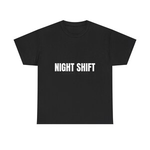 Puede incluir: Camiseta negra con la frase "NIGHT SHIFT" impresa en letras blancas y en negrita en el pecho. La camiseta es de cuello redondo, hecha de un material suave y adecuada para uso casual.