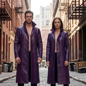Könnte beinhalten: Zwei Personen tragen lange, violette, texturierte Trenchcoats mit hohem Kragen, offener Vorderseite und langen Ärmeln. Jede Person ist mit einer schwarzen Hose und schwarzen Stiefeln bekleidet und steht auf einer Kopfsteinpflasterstraße zwischen Backsteingebäuden.