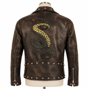 Op de afbeelding: Bruine leren jas met een distressed afwerking, met een groot geborduurd slangenontwerp op de rug. De slang is groen en geel met een rode tong. De jas heeft zilveren studs en ritsen op de mouwen.
