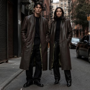 Peut inclure: Deux personnes portant de longs trench-coats en cuir marron foncé sur des chemises et des pantalons noirs. Les manteaux présentent une finition lisse, une silhouette droite et une doublure vert olive visible sur les panneaux intérieurs.