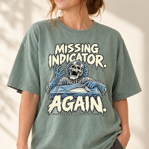 May include: A sage green t-shirt featuring a graphic of a skeleton in surgical scrubs and a hairnet, reaching toward a sterile wrapped tray. The text reads MISSING INDICATOR. AGAIN. STERILE PROCESSING in a distressed, off-white font style.