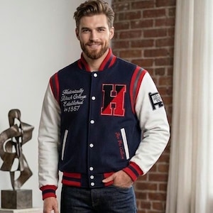 Può includere: Una giacca varsity blu navy con maniche bianche, polsini e colletto a coste a righe rosse e blu navy, e bottoni a pressione bianchi. Il davanti presenta una grande toppa con la lettera H rossa e nera, testo ricamato bianco e due tasche.