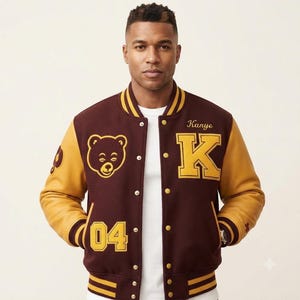 May include: A maroon and gold varsity jacket featuring a bear graphic, the number 04, and the letter K with the name Kanye embroidered on the chest. The jacket has gold sleeves, a button-front closure, and striped ribbed trim on the collar and cuffs.