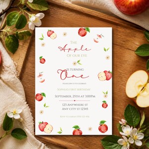 Pode incluir: Um cartão de convite de aniversário retangular com ilustrações em aquarela de maçãs vermelhas, fatias de maçã e flores brancas. O texto diz: The Apple of Our Eye is turning One, Sophia's First Birthday, 25 de setembro às 15h, 123 Anywhere St.