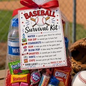May include: A clear plastic gift bag filled with assorted snacks including a water bottle, Fun Dip, Starburst, gum, Blow Pop, Smarties, mints, and chips. A red ribbon ties the top, and a tag reads BASEBALL Survival Kit with game-themed text.