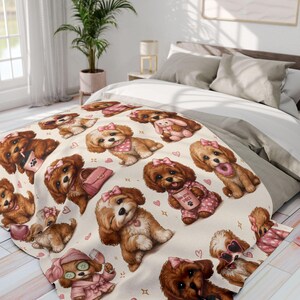 May include: A cream-colored blanket featuring a repeating pattern of cartoon puppies with pink bows, bandanas, and accessories. The puppies are in various poses, some holding purses or wearing pajamas. Hearts and stars are scattered around the dogs.
